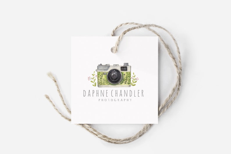 May include: A white tag with a green and white camera illustration with green leaves and red flowers. The text "Daphne Chandler Photography" is below the camera.