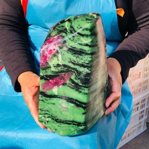 May include: A large, polished mineral specimen featuring a vibrant green base with prominent, wavy black bands and distinct patches of bright magenta-pink inclusions throughout the stone, showcasing a smooth, rounded, and irregular block-like shape.