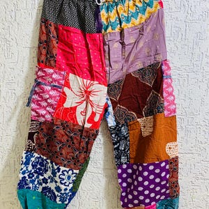 May include: Patchwork pants with a variety of colorful fabric patterns, including floral, geometric, and paisley designs. The pants have an elastic waistband and a drawstring. The color palette includes pink, red, purple, blue, and brown.