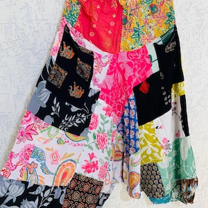 Op de afbeelding: Een patchwork harembroek met een elastische tailleband. De broek heeft een verscheidenheid aan kleurrijke stoffen patches met bloemen-, paisley- en olifantenpatronen. Het kleurenpalet omvat roze, geel, zwart, wit en blauw.