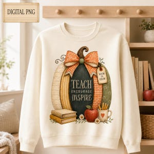 Peut inclure: Un sweat-shirt à col rond couleur crème avec un motif de grosse citrouille ornée d'un nœud à carreaux. La citrouille porte l'inscription TEACH ENCOURAGE INSPIRE. Sous la citrouille se trouvent deux livres empilés, une pomme et un mug.