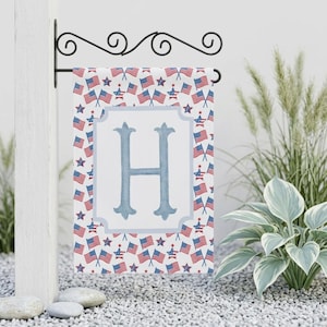 May include: A patriotic garden flag featuring a white background with a light blue letter "H" in the center. The flag is decorated with a pattern of American flags and stars in red, white, and blue.