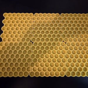 May include: Six yellow silicone mats arranged in a grid, each featuring a repeating hexagonal honeycomb pattern with circular indentations. The mats are uniform in color and design, creating a textured surface with a consistent geometric layout.