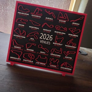 May include: A framed black and red sign displaying the 2026 Formula 1 race venues. The sign features the track layouts and dates for each race, including Melbourne, Miami, and Las Vegas.
