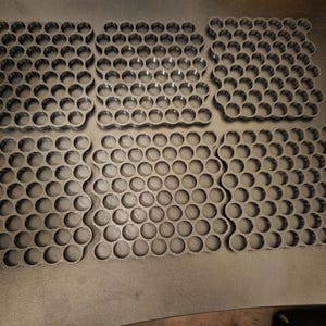 May include: Six black square-shaped organizers featuring a repeating honeycomb pattern of circular cutouts. Each organizer is constructed with a grid of interconnected rings, providing a uniform structure for holding small items in a neat arrangement.