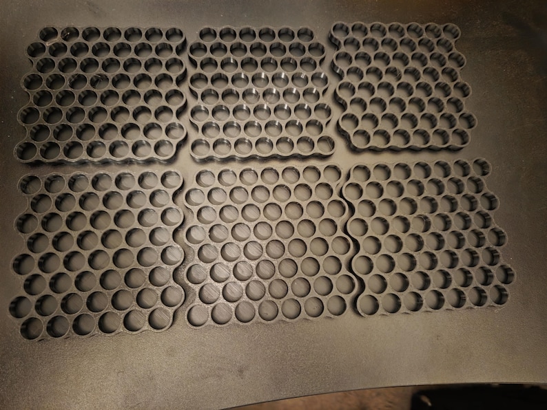 May include: Six black square-shaped organizers featuring a repeating honeycomb pattern of circular cutouts. Each organizer is constructed with a grid of interconnected rings, providing a uniform structure for holding small items in a neat arrangement.