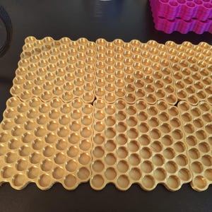 May include: Four square gold-colored trays featuring a repeating honeycomb pattern of circular indentations. Each tray is arranged in a grid formation, showcasing a metallic finish and a structured, geometric design with uniform circular wells.