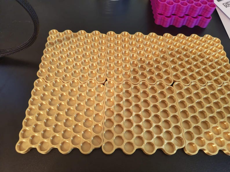 May include: Four square gold-colored trays featuring a repeating honeycomb pattern of circular indentations. Each tray is arranged in a grid formation, showcasing a metallic finish and a structured, geometric design with uniform circular wells.