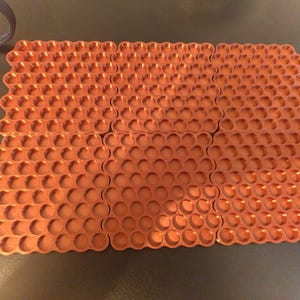 May include: A set of six rectangular copper-colored trays, each featuring a repeating grid of circular indentations. The trays are arranged in a two-by-three formation, showcasing a metallic finish and a uniform honeycomb-like pattern across the surface.