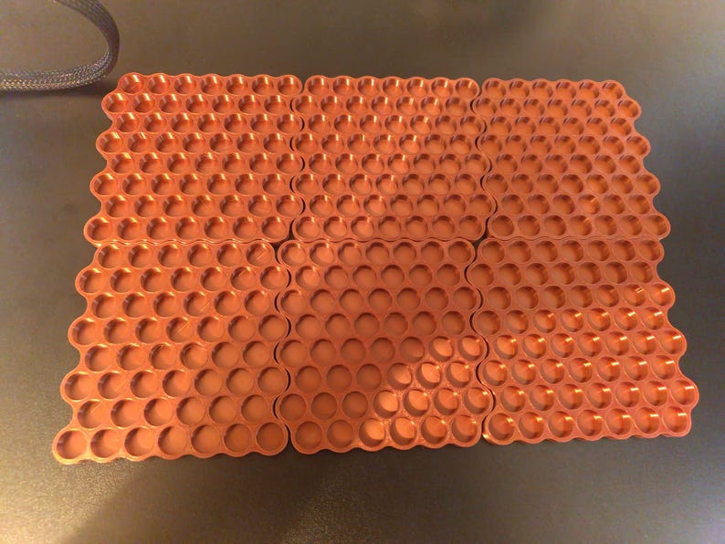 May include: A set of six rectangular copper-colored trays, each featuring a repeating grid of circular indentations. The trays are arranged in a two-by-three formation, showcasing a metallic finish and a uniform honeycomb-like pattern across the surface.
