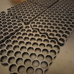 May include: A set of four black 3D printed grid organizers, each featuring a repeating pattern of circular cutouts arranged in a rectangular formation. The organizers are flat with uniform thickness and have a matte finish, designed for storage.