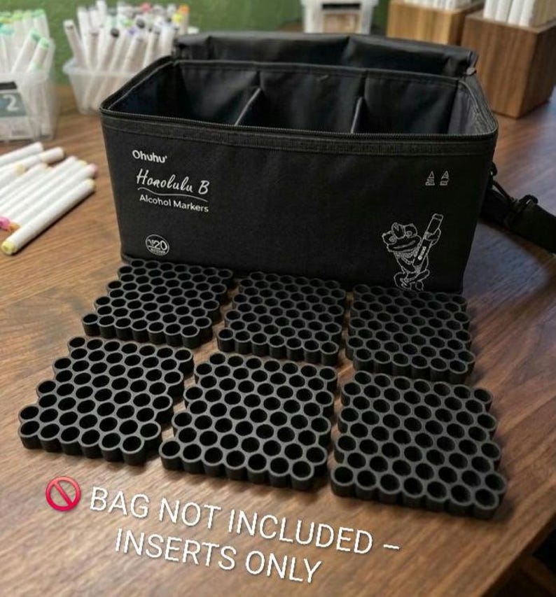May include: A black Ohuhu Honolulu B alcohol marker carrying case with an open top and a white graphic of a frog holding a marker. Six black plastic honeycomb-style grid inserts are arranged in front of the bag on a wooden surface.