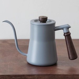 May include: A light gray gooseneck kettle with a wooden handle and lid knob. The kettle has a long, curved spout and is designed for precise pouring. The handle and lid knob are made of dark brown wood.