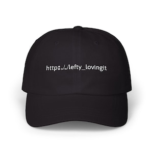 Pode incluir: Um boné de beisebol preto com texto bordado em branco no painel frontal que diz http://lefty_lovingit, com dois pequenos ícones brancos de bola e taco de golfe substituindo as duas barras inclinadas no endereço da web.