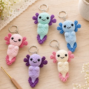 May include: Five crocheted axolotl keychains in various colors including pink, mint green, light blue, purple, and white. Each axolotl features black bead eyes, a stitched smile, external gills, and a tail, all attached to a silver metal keyring.