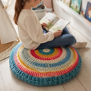May include: A round, hand-crocheted floor cushion featuring concentric rings of yarn in vibrant shades of teal, coral, yellow, and cream. The textured, circular pillow has a thick, chunky stitch pattern and a flat, low-profile design.