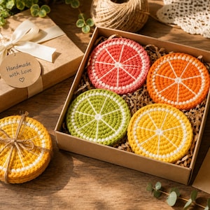 May include: A set of four round, crocheted citrus fruit coasters in pink, orange, green, and yellow, arranged in a brown gift box. A stack of yellow coasters is tied with twine. A tag on the box reads Handmade with Love, and a note reads Especially for you.
