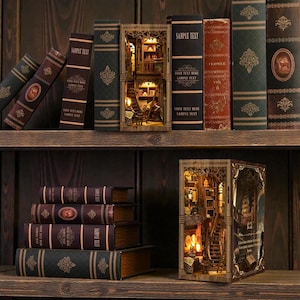 May include: Wooden bookshelf decor with miniature illuminated library scenes. The image shows a collection of decorative books on wooden shelves, including several with intricate cut-out designs revealing interior scenes. The books are in various colors and sizes.