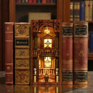 May include: A wooden book nook with a detailed interior scene, illuminated by a warm light. Flanking the nook are antique books with leather covers and gold lettering. The text "Madniy" is visible on one book. The nook is labeled "FAMOUS ITEMS EXHIBITION".