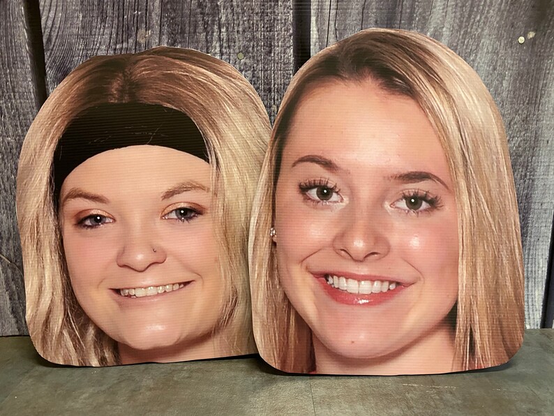 May include: Two cutout cardboard face masks of women with blonde hair. The woman on the left is wearing a black headband. Both women are smiling.