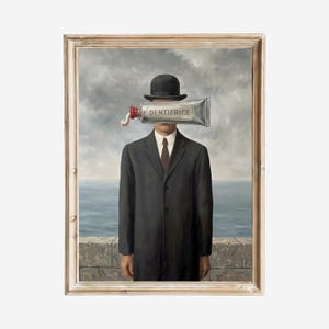 Puede incluir: Pintura surrealista enmarcada que presenta a un hombre con traje negro y bombín. Un tubo de pasta de dientes con la etiqueta "DENTIFRICE" reemplaza la cara del hombre. El fondo muestra un cielo nublado y una vista al mar.