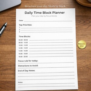 Può includere: Un Daily Time Block Planner bianco con un adesivo dorato "PDF stampabile" su una superficie di legno. Il planner include sezioni per data, priorità principali, blocchi temporali, regole di concentrazione e note. Il testo "Structure your day, block by block" è in alto.