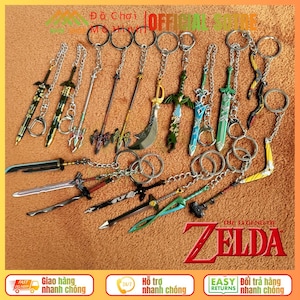 Może przedstawiać: Kolekcja miniaturowych breloków do kluczy w kształcie mieczy o różnych wzorach i kolorach, w tym złotym, srebrnym, zielonym i niebieskim. Breloki są przymocowane do srebrnych łańcuszków i kółek. Widoczny jest napis "THE LEGEND of ZELDA".