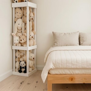 Peut inclure: Unité de rangement d'angle blanche remplie d'animaux en peluche, dont des ours en peluche, des lapins et un panda. L'unité est à côté d'un lit avec une couette et des oreillers de couleur claire. La pièce a des murs clairs et un sol en bois.