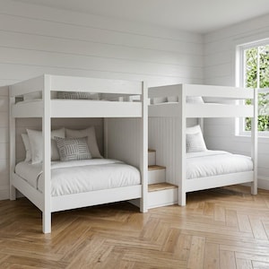 May include: A white wooden bunk bed set featuring two levels with integrated stairs between the beds. Each bed is dressed with white bedding and a single gray patterned throw pillow. The structure has a vertical slat design on the headboards.