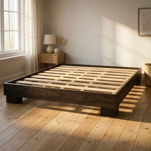Puede incluir: Una estructura de cama de plataforma de madera teñida oscura con una base de listones. La estructura de la cama es rectangular con un perfil bajo y se asienta sobre cuatro patas cuadradas. Los listones son de madera natural. La cama está en una habitación bien iluminada con pisos de madera.