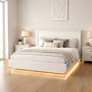 May include: A modern white bed frame with a matching headboard, adorned with pillows and a neutral-toned blanket. The bed is illuminated by a warm, soft light underneath, creating a cozy ambiance. Two white nightstands with lamps flank the bed.