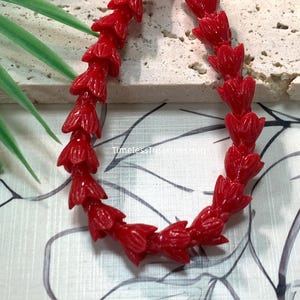 May include: A strand of bright red beads, each carved into the shape of a small, closed flower bud. The beads are arranged in a curved line, showcasing a glossy finish and uniform design. The text Red and TimelessTreasuresMug are visible.
