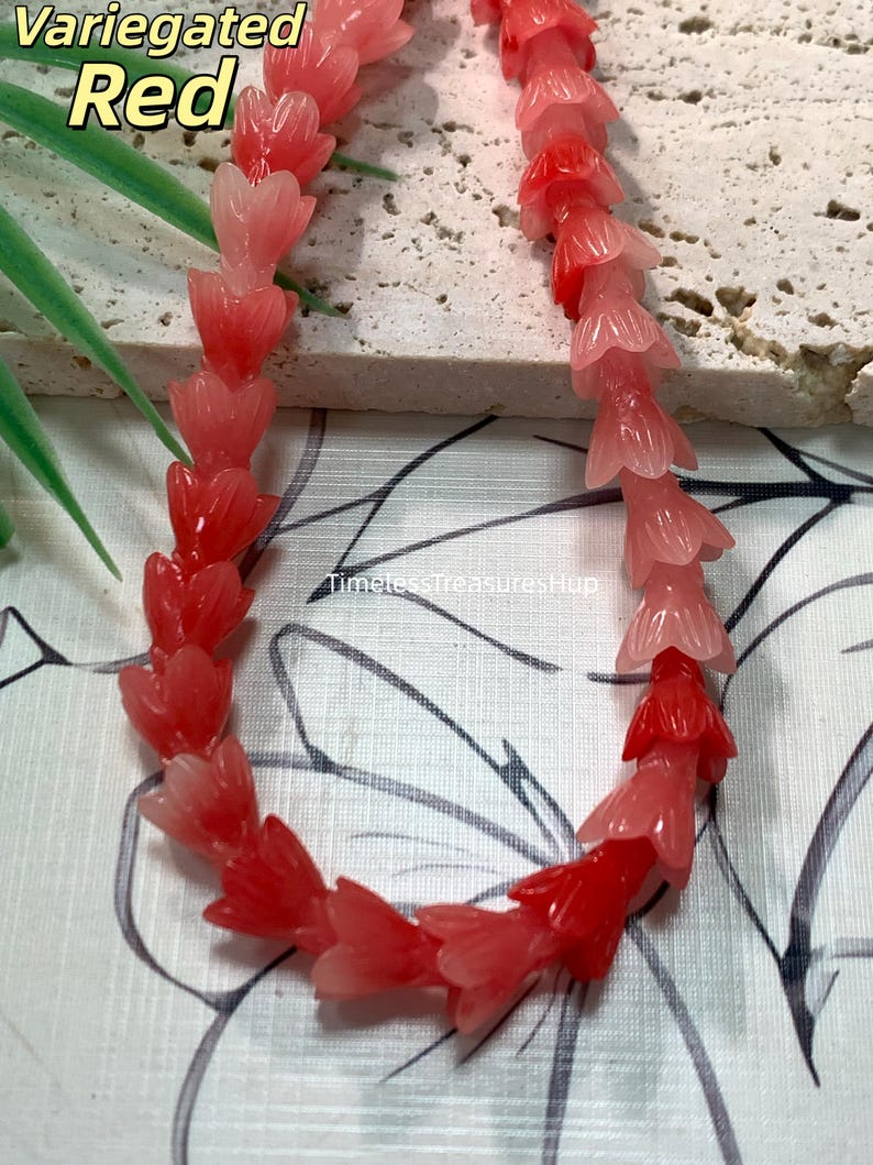 May include: A strand of beads shaped like small tulip flowers in variegated shades of red and pink. The beads transition from deep red to lighter coral and pale pink hues. The text Variegated Red and TimelessTreasuresHup are visible.
