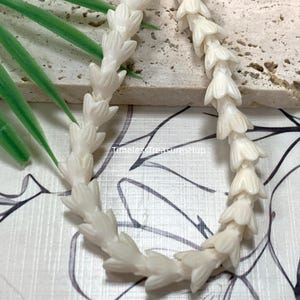 May include: A strand of off-white beads carved into the shape of small, layered flower buds. The beads are strung together in a continuous line. The text "White" appears in the upper left corner, and "TimelessTreasuresHup" is printed in the center.