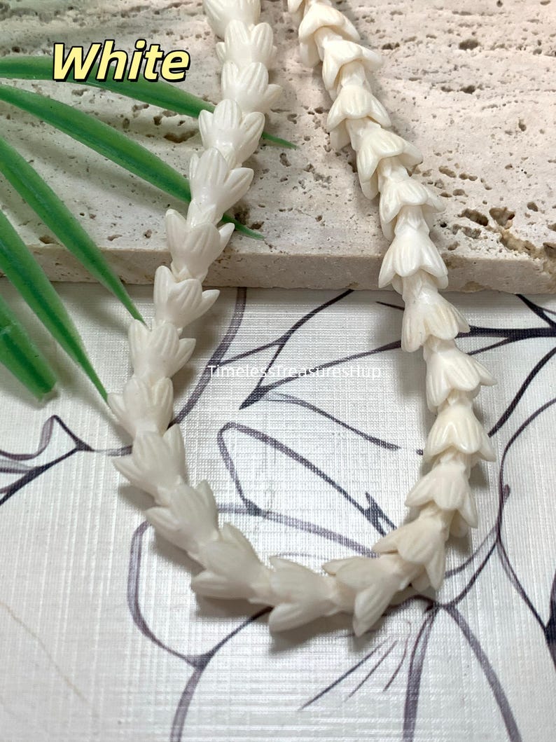 May include: A strand of off-white beads carved into the shape of small, layered flower buds. The beads are strung together in a continuous line. The text "White" appears in the upper left corner, and "TimelessTreasuresHup" is printed in the center.