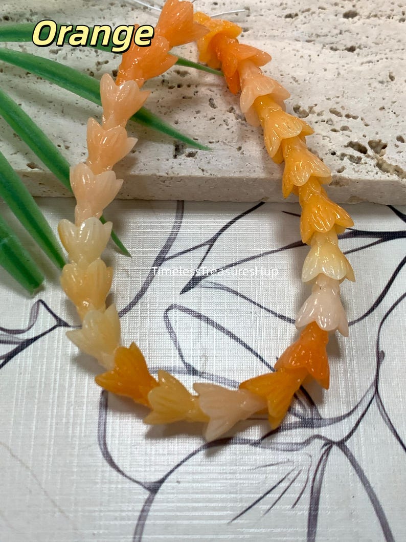 May include: A bracelet composed of translucent, flower-shaped beads in varying shades of orange, ranging from pale peach to deep amber. The beads are strung together in a circular pattern. The text "Orange" and "TimelesstreasuresHup" are visible.