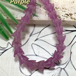 May include: A strand of transparent purple beads shaped like small flower buds. The beads are arranged in a curved line. The text Transparent Purple is visible in the upper left corner, and the text TimelessTreasuresHub is visible in the center.