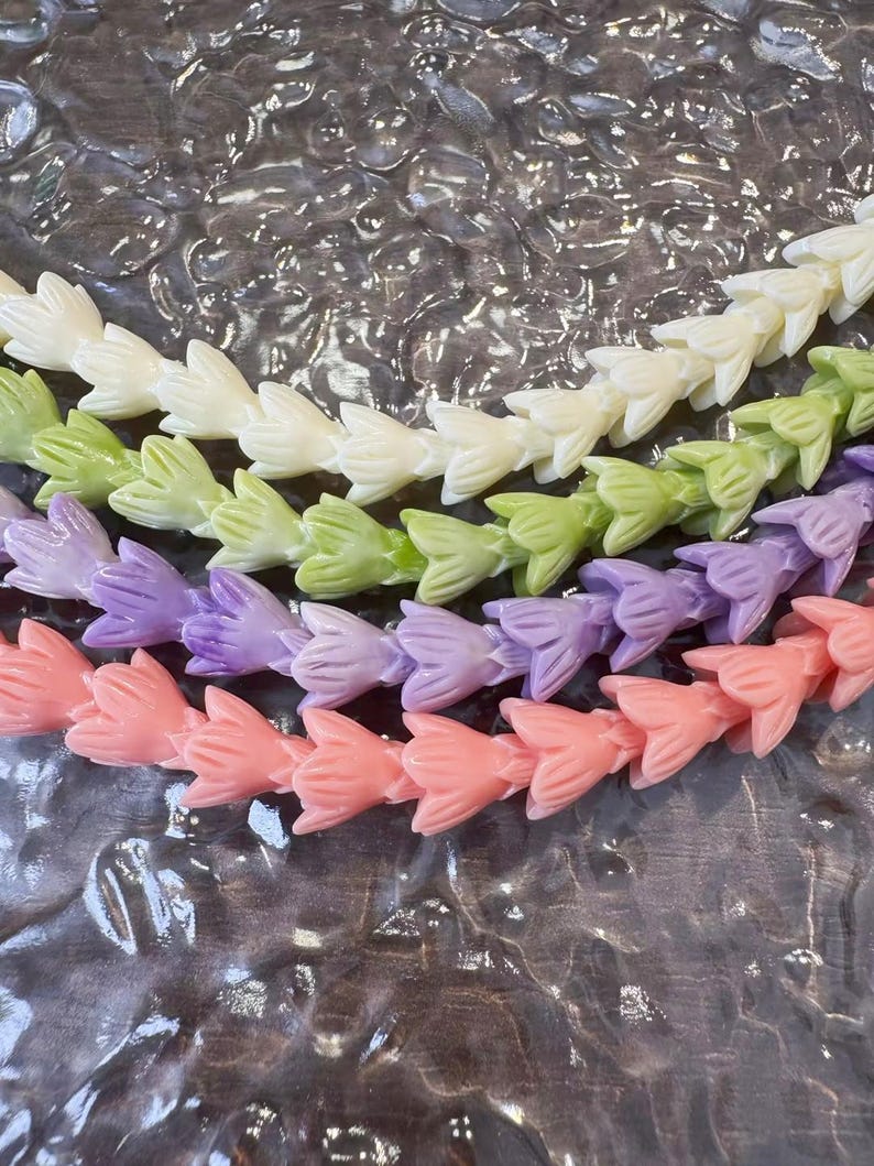 May include: Four strands of flower-shaped beads arranged in parallel rows. The top strand is cream, the second is light green, the third is lavender, and the bottom strand is coral pink. Each bead features a carved petal design in a matte finish.