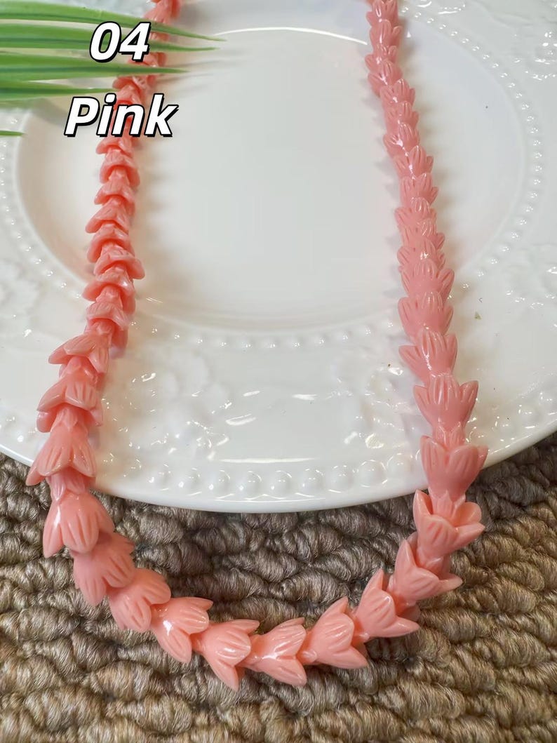 May include: A necklace composed of light pink beads, each carved into the shape of a small flower or tulip bud. The beads are strung together in a continuous strand, creating a uniform floral pattern throughout the length of the jewelry piece.