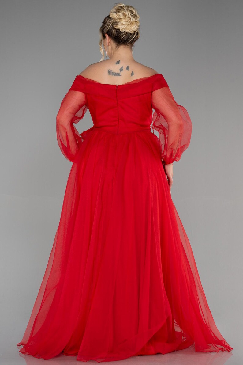 May include: A vibrant red, floor-length gown with an off-the-shoulder design and sheer, long sleeves. The dress has a full skirt and is made of a light, possibly chiffon-like material. The back of the dress is visible, showing the bodice's construction.