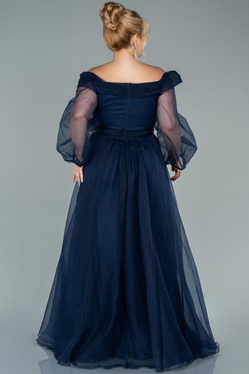 May include: A navy blue formal gown with an off-the-shoulder neckline and sheer, long sleeves. The dress features a fitted bodice and a flowing, floor-length skirt. The back of the dress has a zip closure.