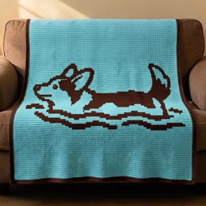 May include: A light blue crochet blanket featuring a dark brown pixelated graphic of a corgi dog swimming. The blanket has a solid dark brown border that frames the light blue center. The design shows the dog in profile with its head and tail visible.