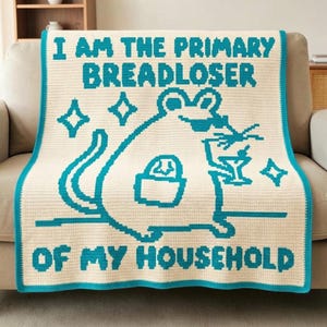 May include: A cream-coloured crochet blanket featuring a teal pixelated design of a mouse holding a martini glass. The text reads I AM THE PRIMARY BREADLOSER OF MY HOUSEHOLD. The blanket has a teal border and includes small star-shaped accents.