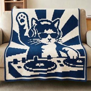 Könnte beinhalten: Eine rechteckige Häkeldecke mit einem zweifarbigen Grafikdesign in Marineblau und Creme. Das Muster zeigt eine Katze mit Sonnenbrille und Kopfhörern, die hinter einem DJ-Plattenspieler-Setup mit einem Sonnenstrahlen-Hintergrundmotiv positioniert ist.