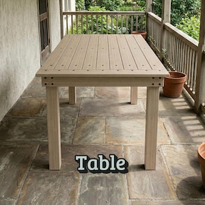 Op de afbeelding: Een lichtbruine rechthoekige tafel met een lattenblad en vier vierkante poten. De tafel heeft een natuurlijke houtnerf en staat op een stenen terras. Het woord "Table" wordt in zwart en wit onderaan de tafel weergegeven.