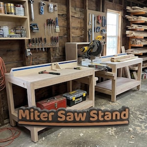 Op de afbeelding: Een lichtgekleurde houten verstekzaagstandaard met een vlak werkoppervlak, een blauwe rail en een onderste plank. Een geel-zwarte verstekzaag is aan de rechterkant gemonteerd. De tekst "Miter Saw Stand" staat op de voorgrond.