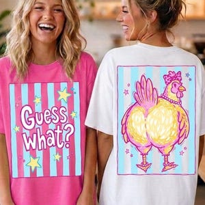 May include: Two women wearing matching t-shirts. One shirt is pink with the text "Guess What?" and blue and yellow accents. The other shirt is white with a cartoon chicken design in pink, yellow, and blue.