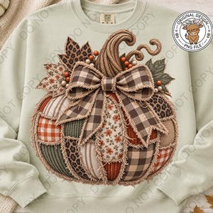 May include: A light green crewneck sweatshirt featuring a large central graphic of a pumpkin made from various fabric patches including plaid, leopard print, and floral patterns. The pumpkin is topped with a large brown plaid bow and rope stem.