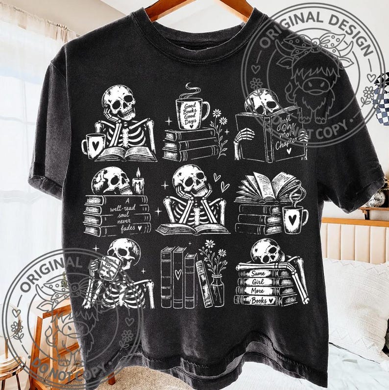 May include: A black short-sleeve t-shirt featuring a white graphic print of skeletons reading books and drinking from mugs. The design includes stacks of books, flowers, and text that reads Good Books Good Days, A well-read soul never fades, and Same Girl More Books.