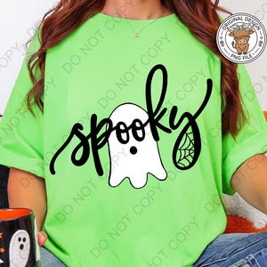 Op de afbeelding: Een fel limoengroen t-shirt met een zwart grafisch ontwerp met het woord spooky in cursief schrift. Het ontwerp bevat een witte geestillustratie met een zwarte stip als oog en een klein spinnenwebdetail op de letter y.